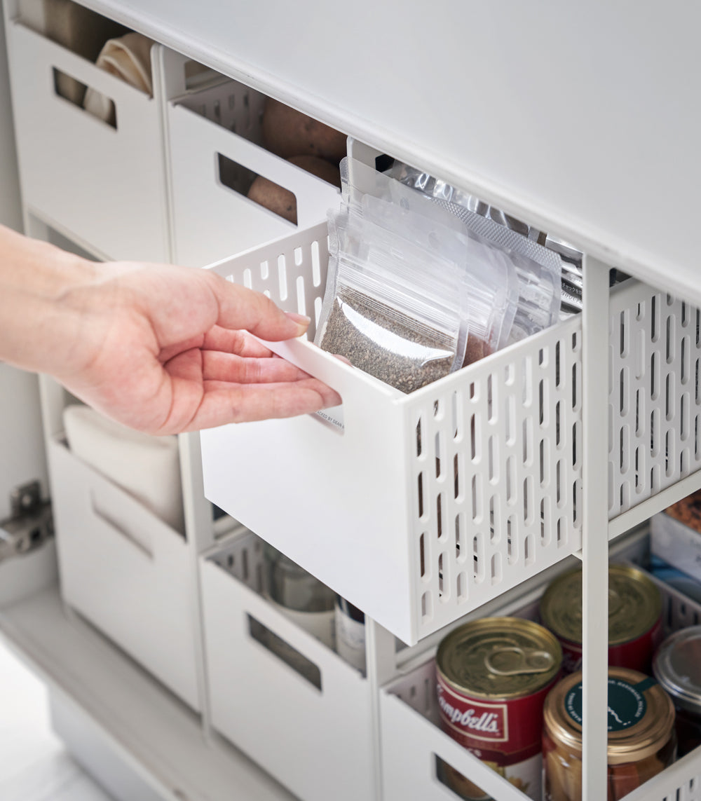 Three two-tier storage bins are displayed in a lower cabinet. Both levels of each hold various food products. A model is sliding the upper level of one out to show its accessibility.