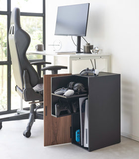 The black video game storage cabinet is placed next to the home office desk. With the door opened, it showcases video games, controllers, and headsets neatly organized inside, demonstrating its functionality and seamless integration into the room's decor view 16