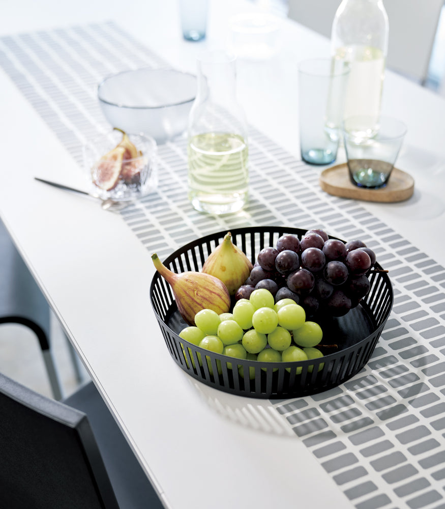View 7 - Black Fruit Basket holding figs and grapes on dining table by Yamazaki Home.