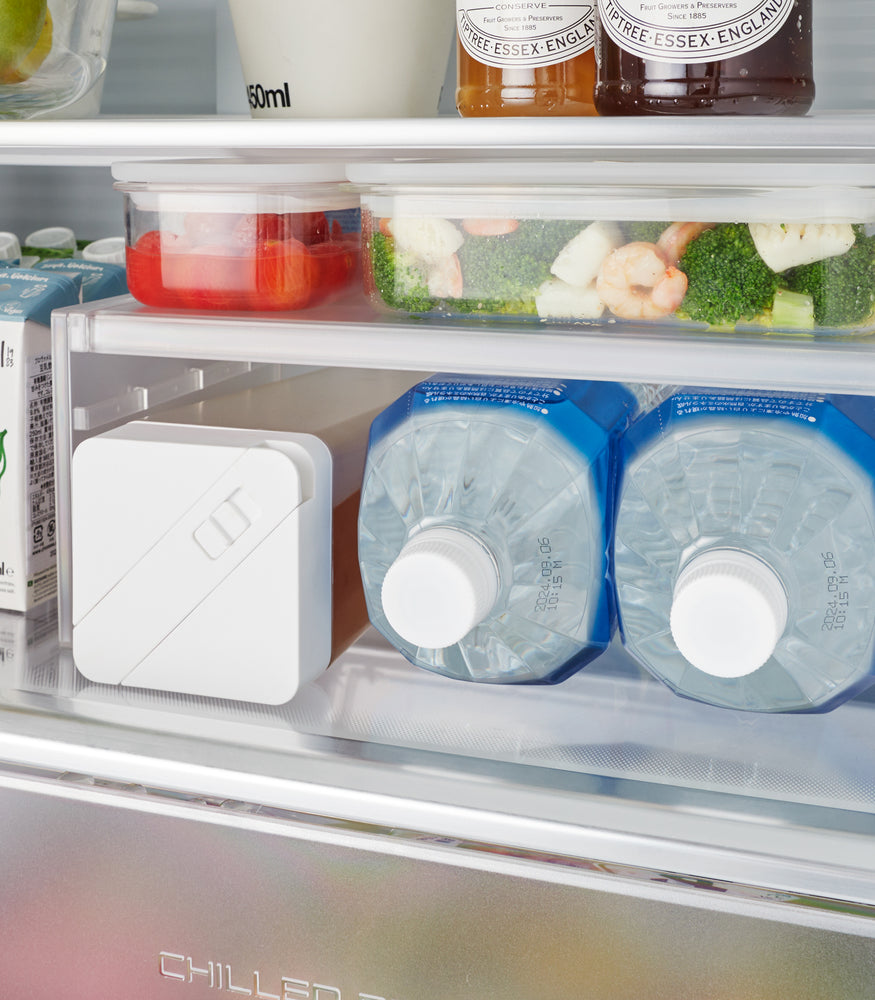 View 4 - Detail of a white Expandable Refrigerator Riser Shelf by Yamazaki Home in a fridge, showcasing its capacity to double storage areas for food items.