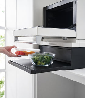 Image of the Countertop Drawer with Pull-Out Shelf by Yamazaki Home in black from the side. The shelf is pulled out and holding containers of food. A small microwave sits atop the unit. view 12