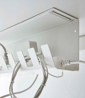 Close-up of Under-Desk Cable Organizer in white by Yamazaki Home mounted under a desk holding a power strip. view 7