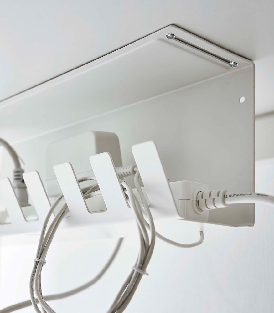 View 7 - Close-up of Under-Desk Cable Organizer in white by Yamazaki Home mounted under a desk holding a power strip.