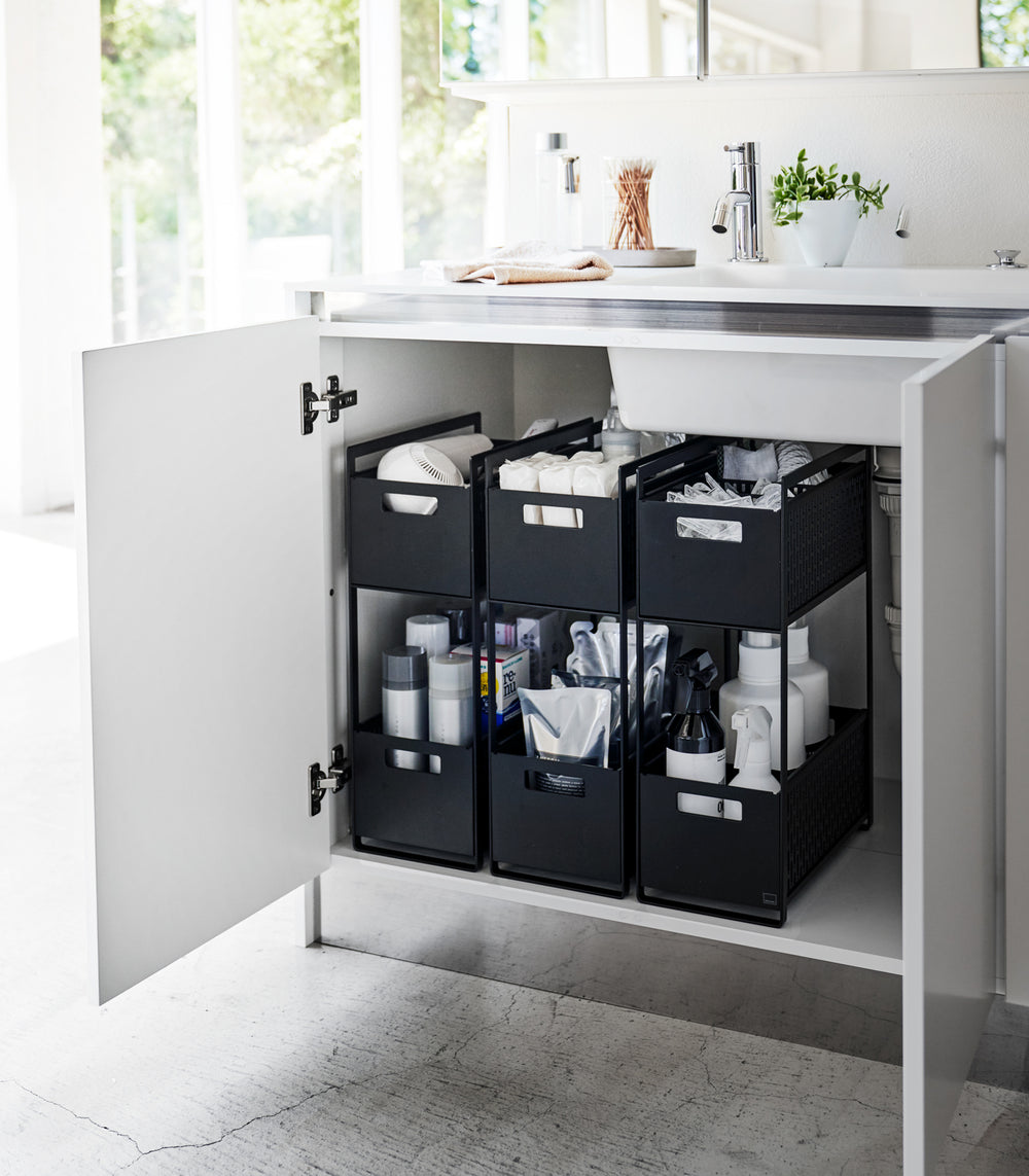 Three black two-tier storage bins are displayed in an under-a-sink cabinet. Both levels of each hold various cleaning products and supplies.