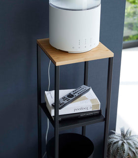 Closeup of Yamazaki black Pedestal Stand with an air purifier, tv remote and books view 15