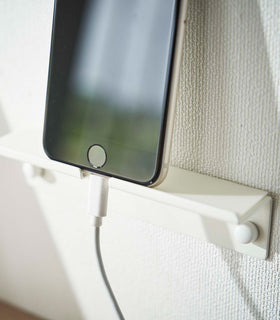 An iPhone securely mounted on a wall, showcasing its screen while positioned vertically. The charger cord is neatly threaded through a designated opening in the mount, ensuring a streamlined appearance view 6