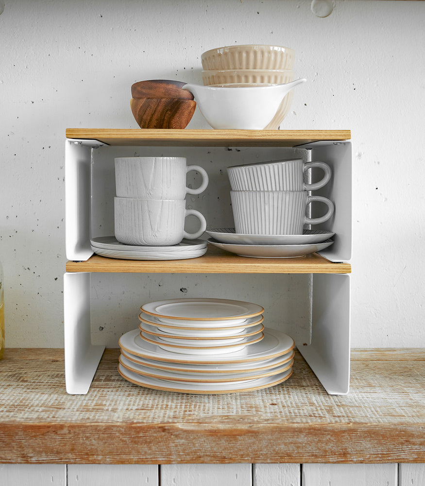View 15 - Front view of white Stackable Countertop Shelves stacked together holding cups and dishes by Yamazaki Home.