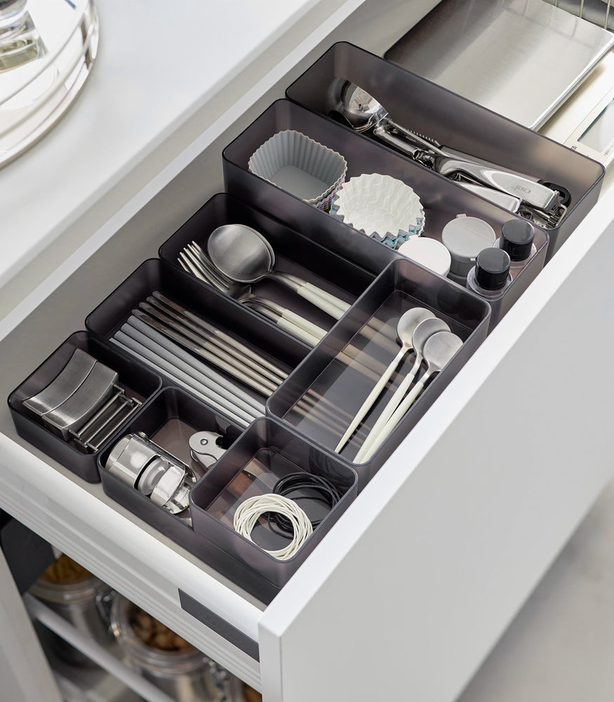 View 29 - Four different sizes of stackable clear organizers in black—small, medium, large, and deep—are neatly placed in a kitchen drawer. They effectively organize various items such as cutlery, bottle openers, and small trays, showcasing their versatility and stackability