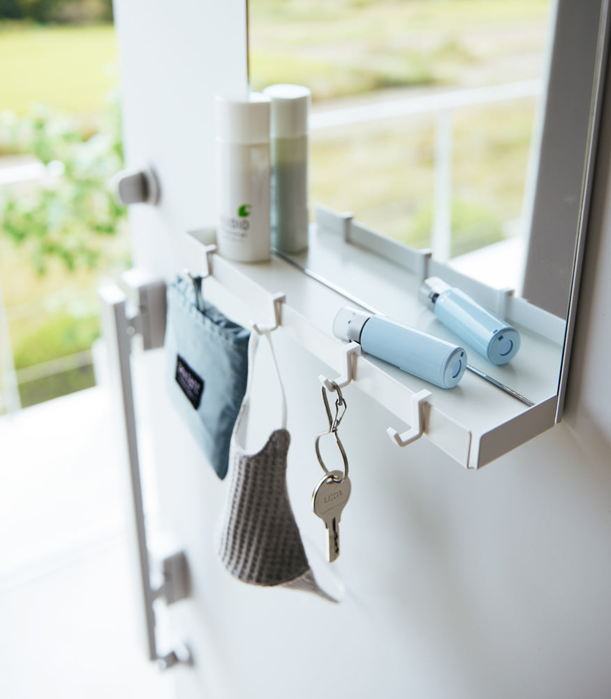 View 3 - A close up of a white Yamazaki Magnetic Mirror With Storage Rack attached to a door with a hanging bag, mask, and key.