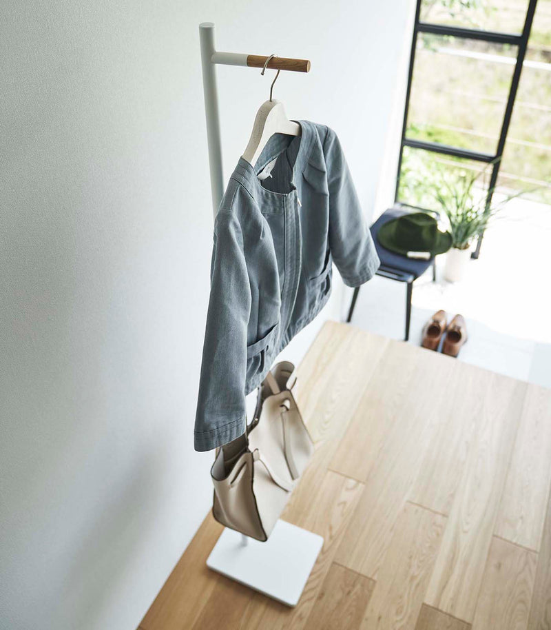 Top-down side view of white Yamazaki Coat Rack with a purse and jacket hanging on it in an entryway
