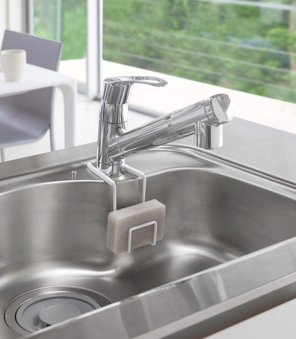 White Faucet-Hanging Sponge holder attatched to sink holding sponge by Yamazaki Home.