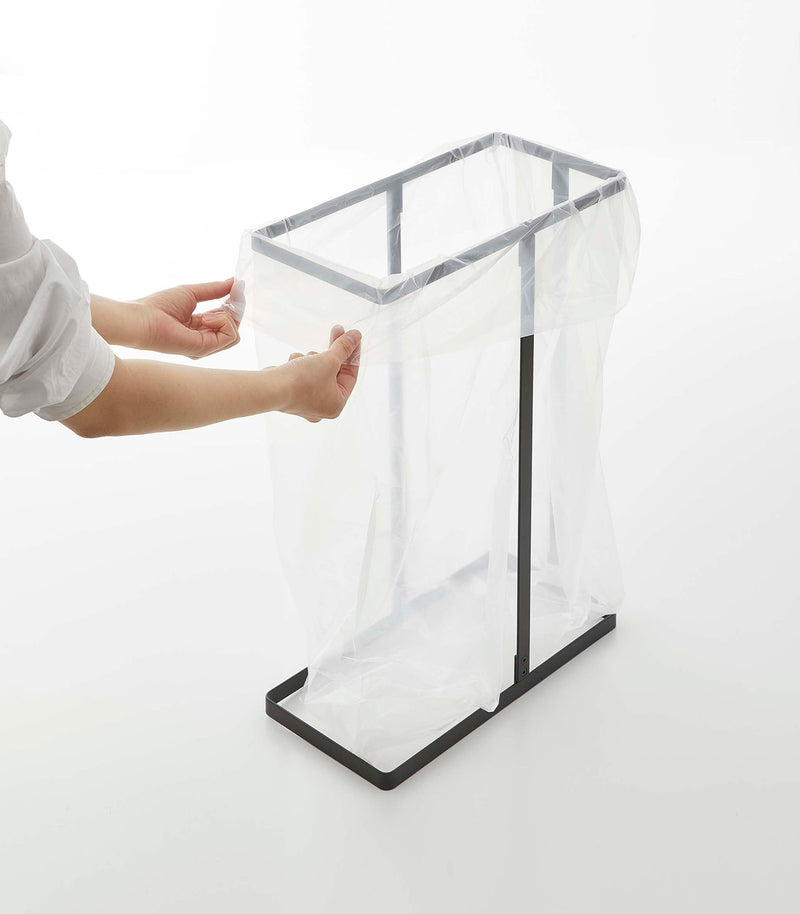 Black Yamazaki Home Lidded Garbage Bag Holder with a bag being put inside