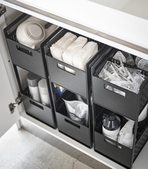 Three black two-tier storage bins are displayed in an under-a-sink cabinet. Both levels of each hold various cleaning products and supplies.