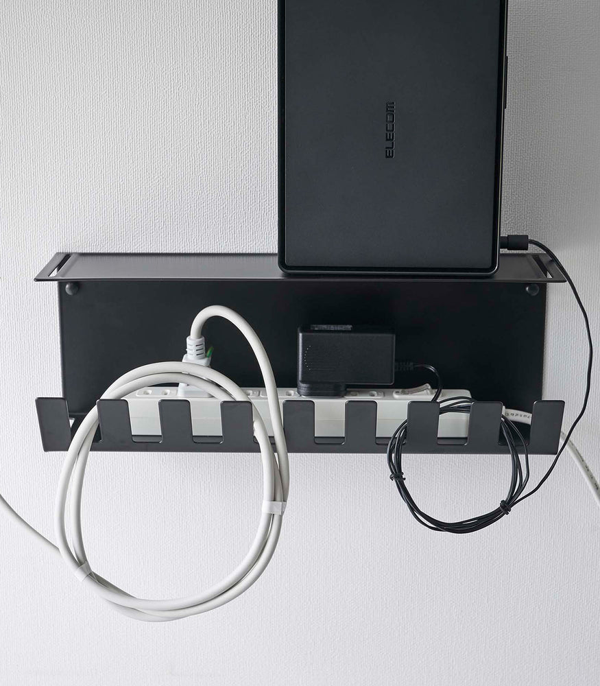 View 15 - Close-up of Under-Desk Cable Organizer in black by Yamazaki Home mounted on a wall holding cables and a router.
