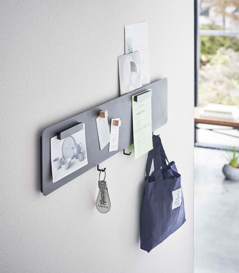 Side view of a Yamazaki black Magnetic Wall Panel with keys and a bag hanging from hooks