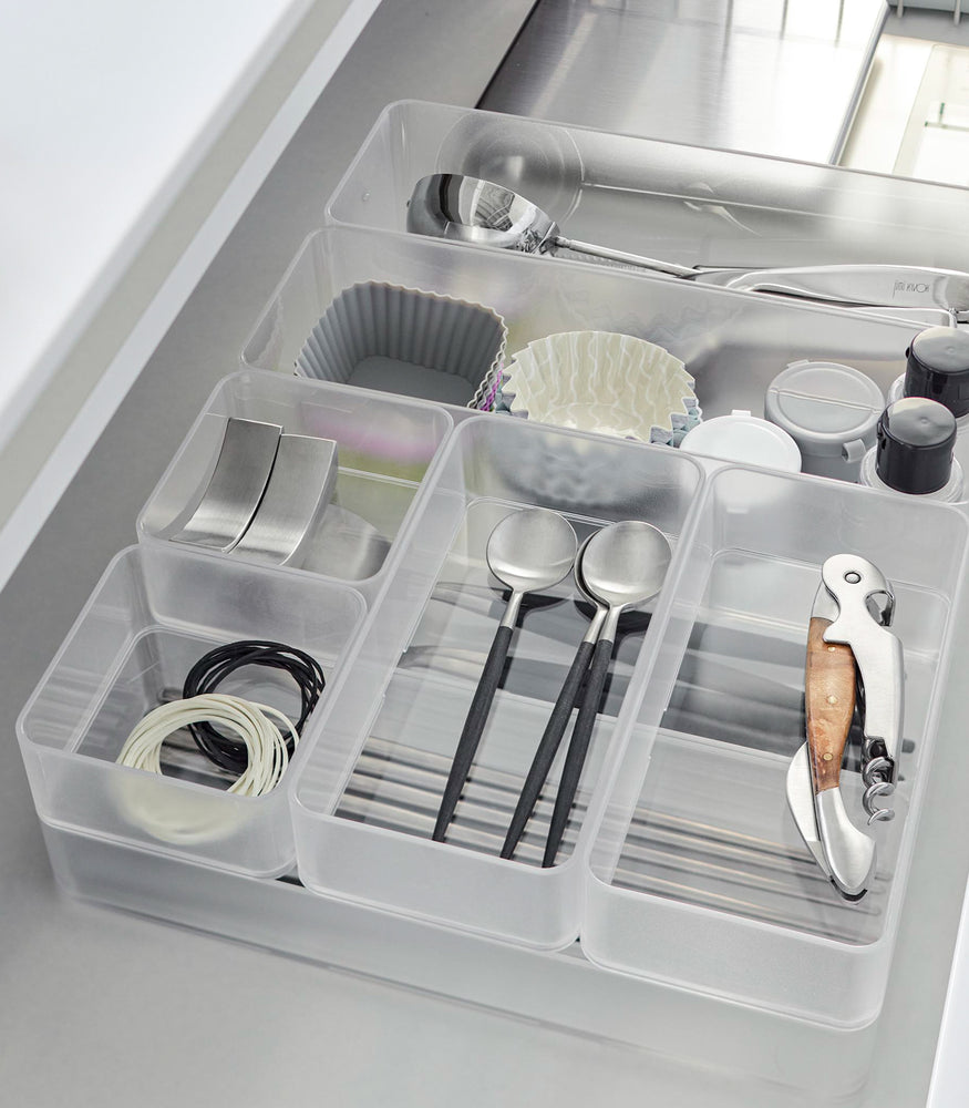 View 53 - Close-up image of four different sizes of stackable clear organizers—small, medium, large, and deep—neatly placed in a kitchen drawer. They effectively organize various items such as cutlery, bottle openers, and small trays, showcasing their versatility and stackability.