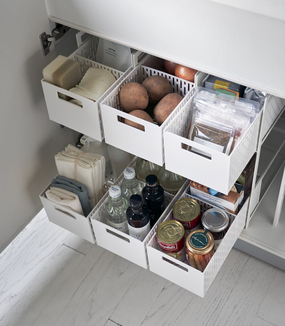 Three two-tier white storage bins are displayed in a lower cabinet. The first houses cleaning supplies, the other two hold pantry items. All levels of the storage bin are pulled out mid-way to show its storage possibilities.