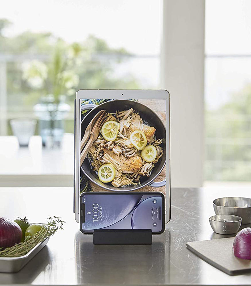 Front view of black Phone and Tablet Stand holding phone and tablet on kitchen counter by Yamazaki Home.