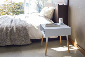 Side view of white Storage Table holding books, phone, and clock in bedroom by Yamazaki Home. view 4