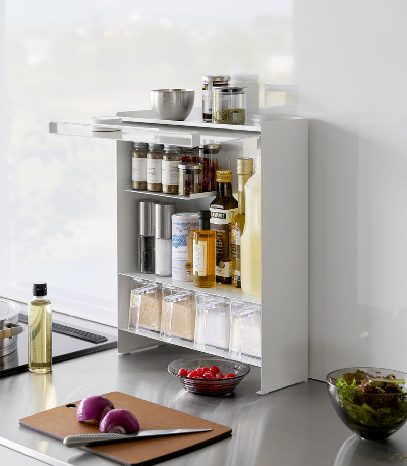 Diagonal view of the Concealable Spice Rack in white by Yamazaki Home with the front panel open, showing various spices and condiments inside.