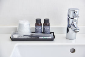 Front view of flat black Accessory Tray holding toothbrush, cup, and soap on bathroom sink counter by Yamazaki Home. view 20