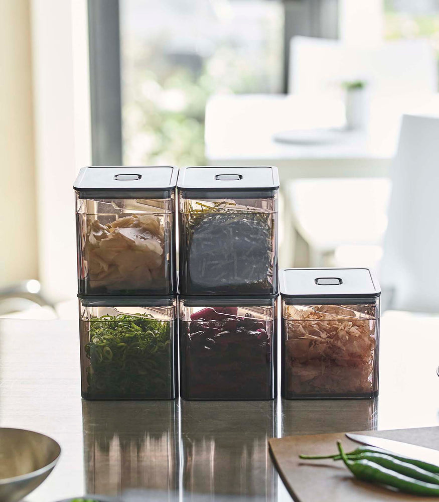 View 13 - Front view of Black Vacuum-Sealing Food Containers w. Tongs stacked on kitchen countertop by Yamazaki Home.