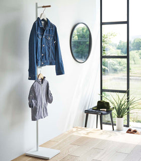 White Yamazaki Coat Rack placed in an entryway with a jacket and a child's shirt hanging on it view 3