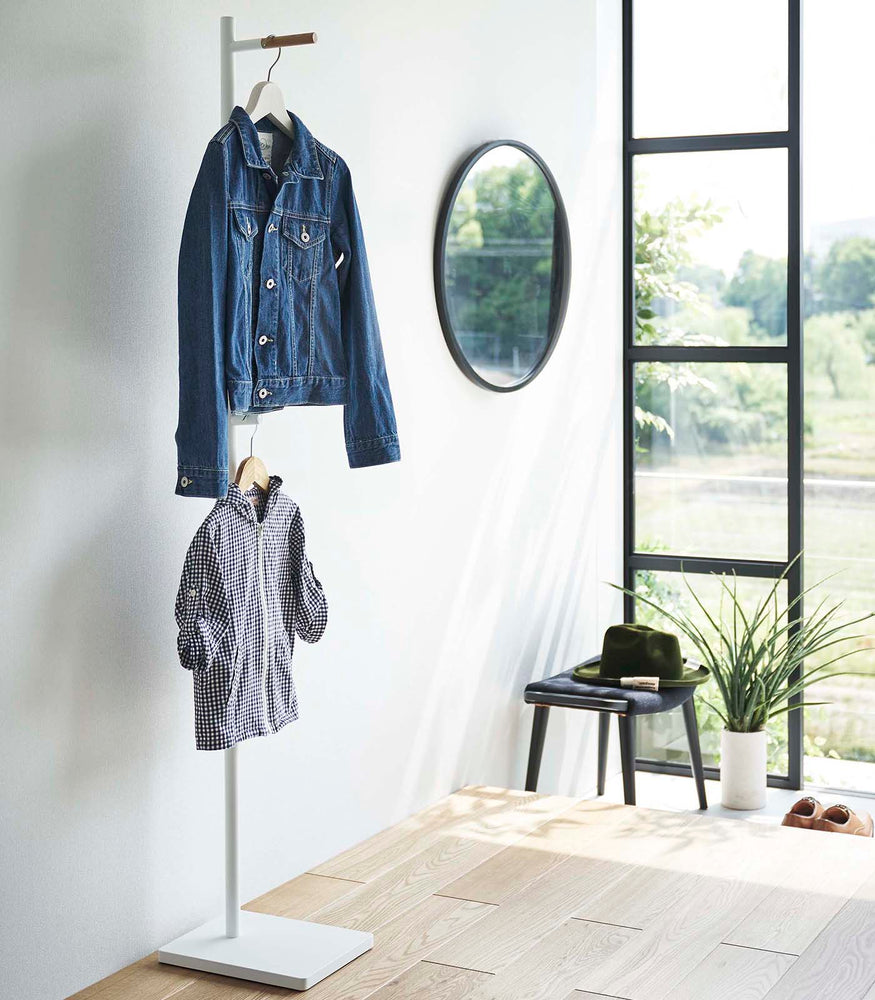View 3 - White Yamazaki Coat Rack placed in an entryway with a jacket and a child's shirt hanging on it