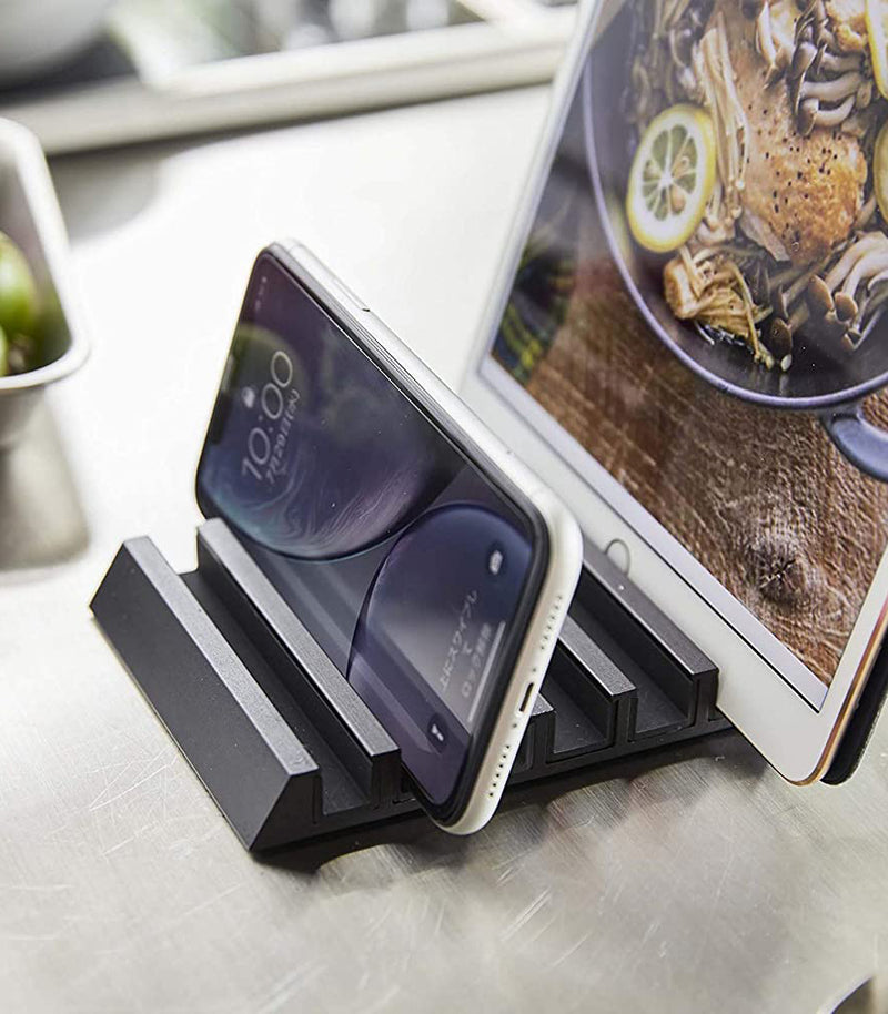 Close up view of black Phone and Tablet Stand holding phone and tablet on counter by Yamazaki Home.