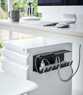 Magnetic Under-Desk Cable Organizer in black by Yamazaki Home mounted on the side of a file cabinet holding a power strip and phone. view 10