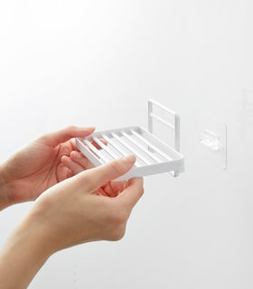 Hands installing Yamazaki Home's white Traceless Adhesive Soap Tray on a bathroom wall, demonstrating its ease of use. view 6