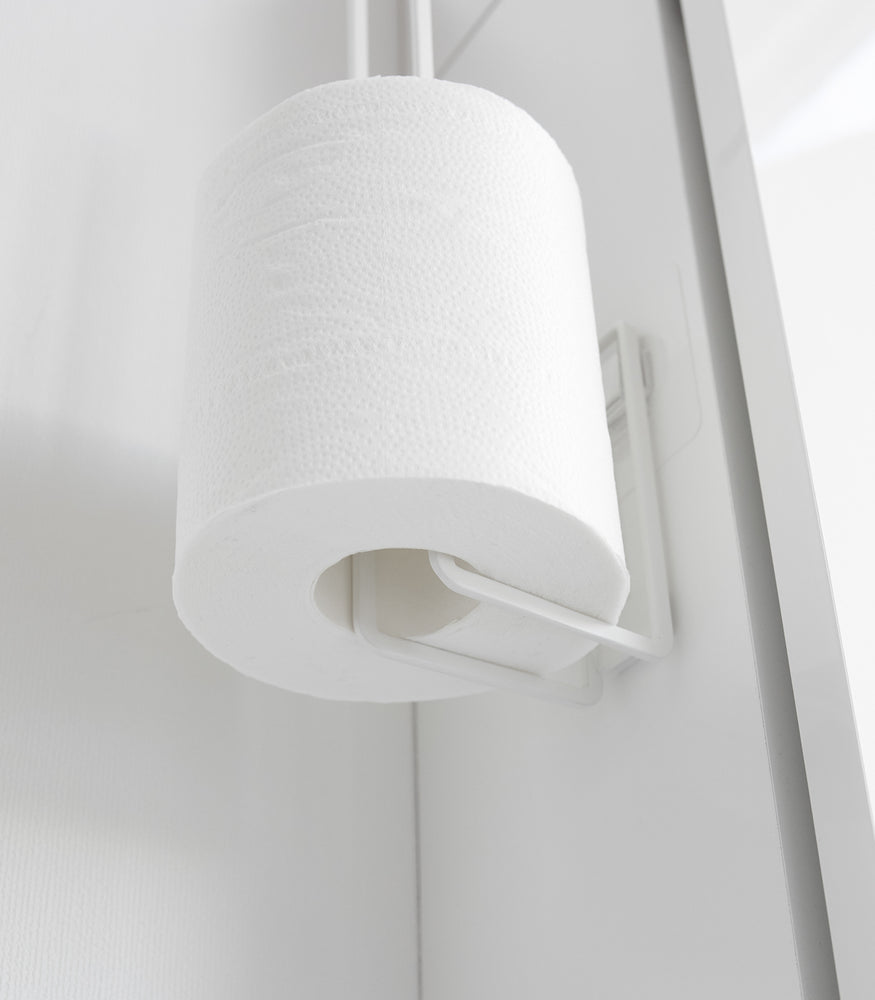 View 6 - Close up of underside of white Yamazaki Home Traceless Adhesive Toilet Paper Holder with a roll stored