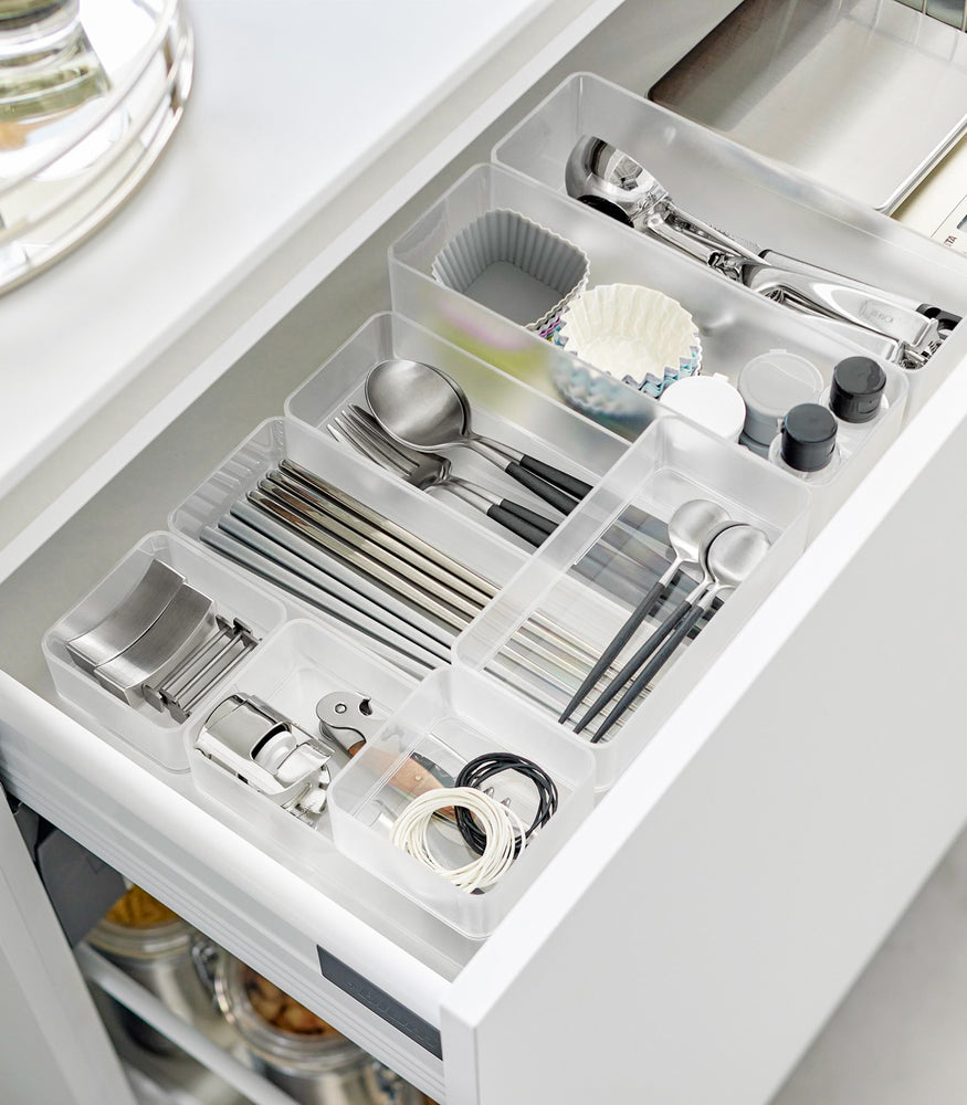 View 36 - Four different sizes of stackable clear organizers—small, medium, large, and deep—are neatly placed in a kitchen drawer. They effectively organize various items such as cutlery, bottle openers, and small trays, showcasing their versatility and stackability