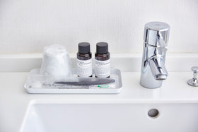 Front view of flat white Accessory Tray holding soap, cup, and toothbrush on sink countertop by Yamazaki Home. view 15