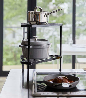 Black Two-Tier Corner Riser holding pot and saucepan next to stovetop by Yamazaki Home. view 8