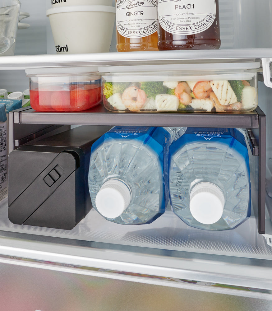 View 11 - Detail of a Black Expandable Refrigerator Riser Shelf by Yamazaki Home in a fridge, showcasing its capacity to double storage areas for food items.