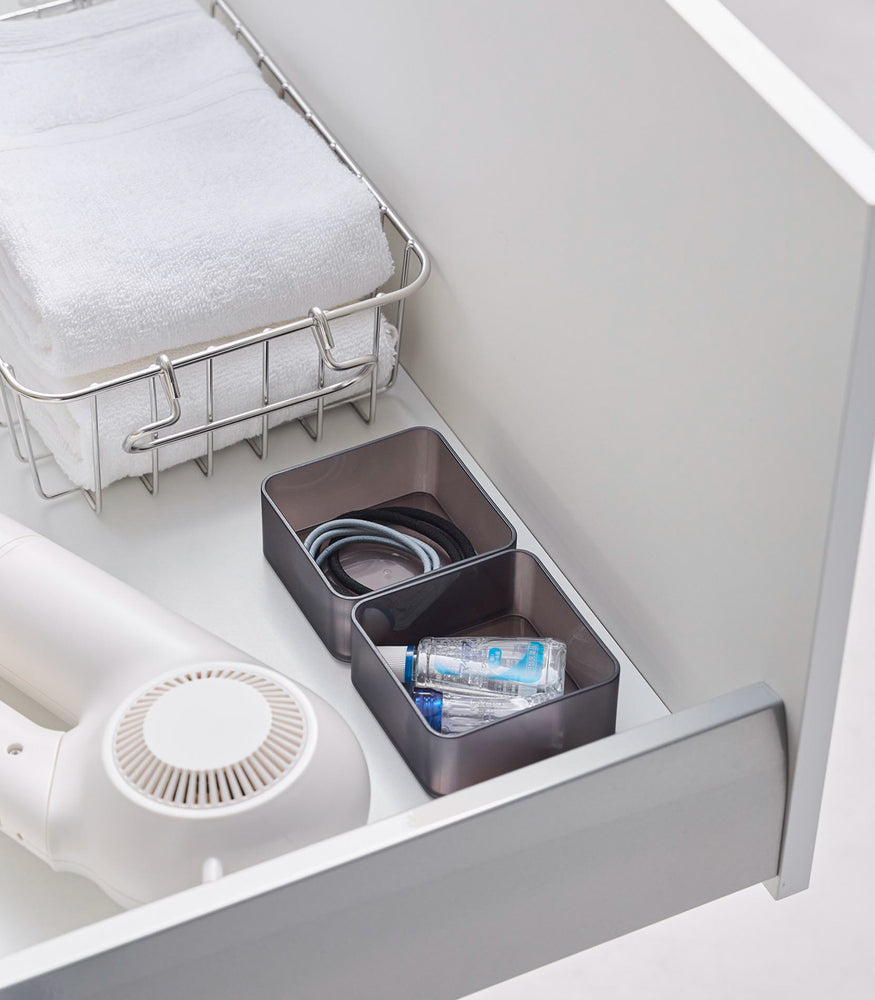 View 12 - Two small stackable clear organizers in black are placed in a bathroom drawer, organizing small items like tiny bottles