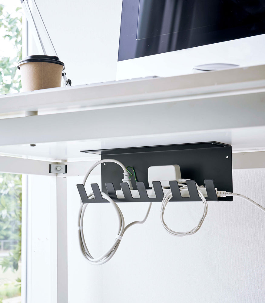 View 11 - Under-Desk Cable Organizer in black by Yamazaki Home mounted under the desk holding a power strip.