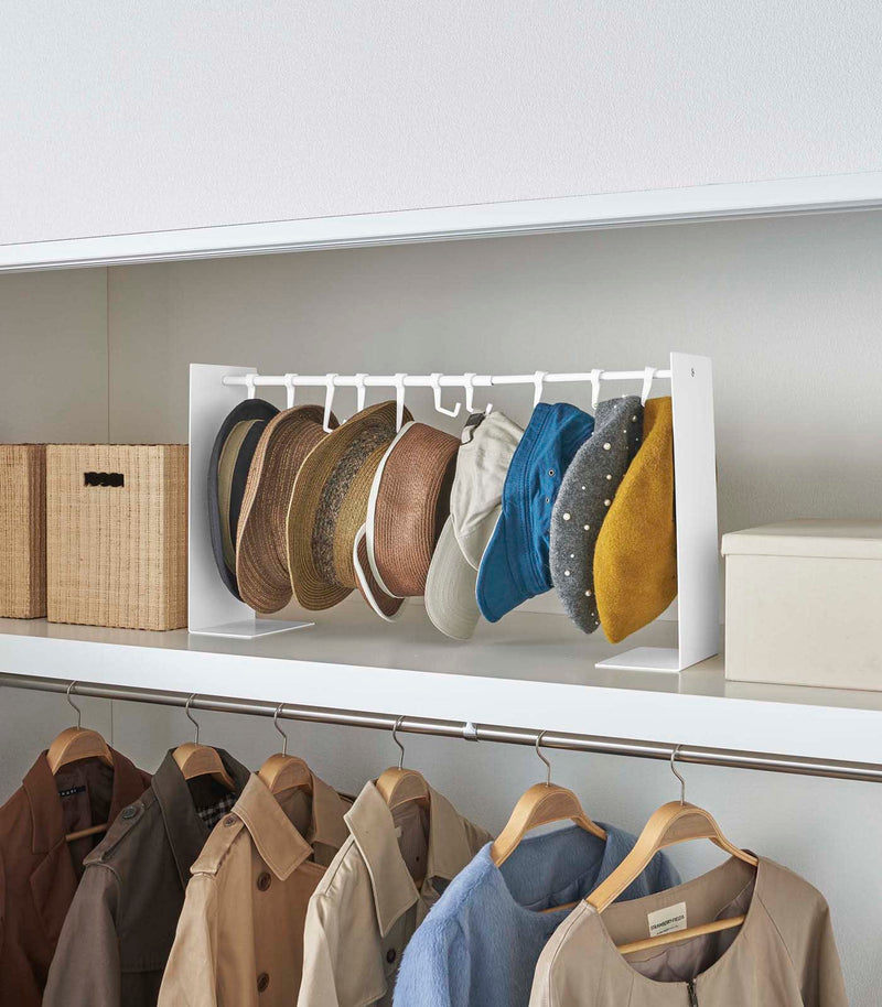 White Yamazaki Home hat rack hanging a variety of hats in a closet