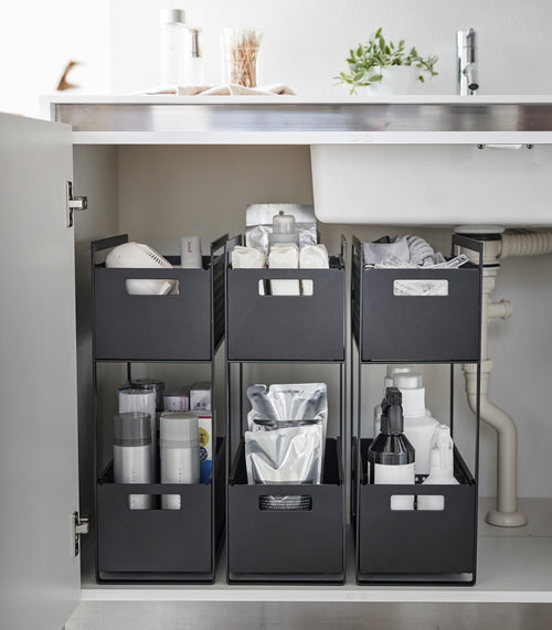 Three black two-tier storage bins are displayed in an under-a-sink cabinet. Both levels of each hold various cleaning products and supplies.