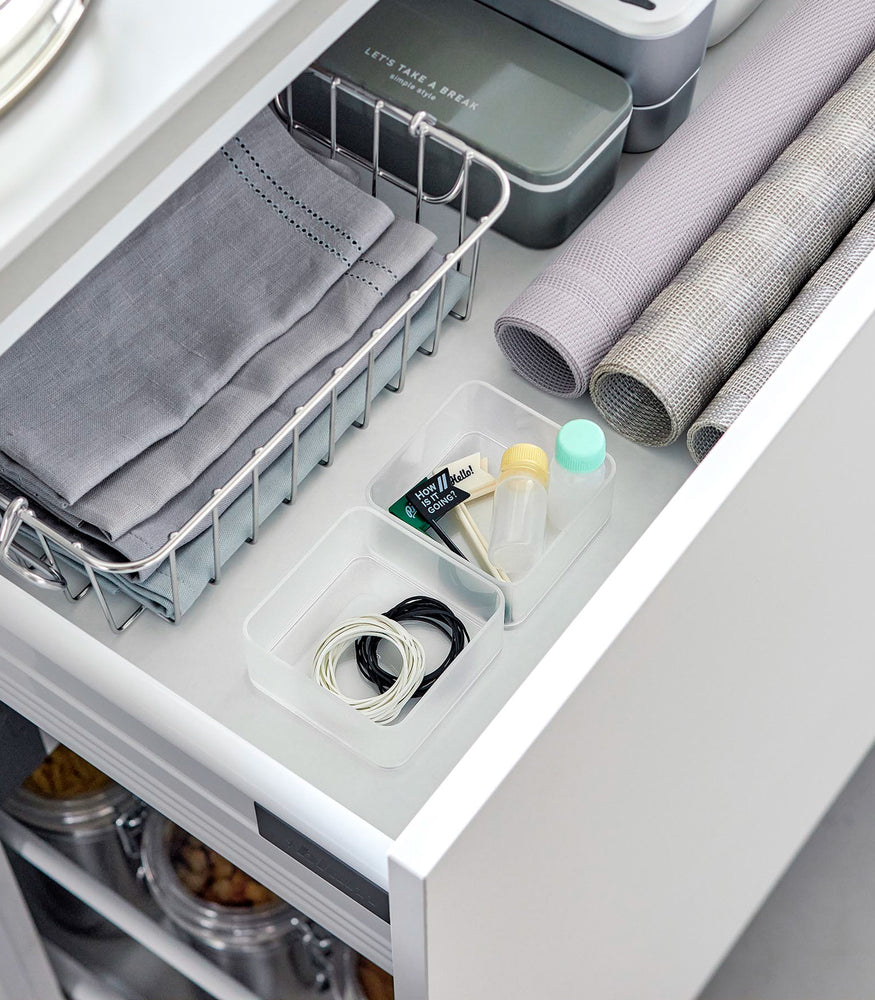 View 31 - Two small stackable clear organizers are placed in a kitchen drawer, organizing small items like strings and tiny sauce bottles