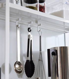 Close-up image of the hooks on the Two-Tier Countertop Rack by Yamazaki Home in white with measuring spoons hanging from them. view 8