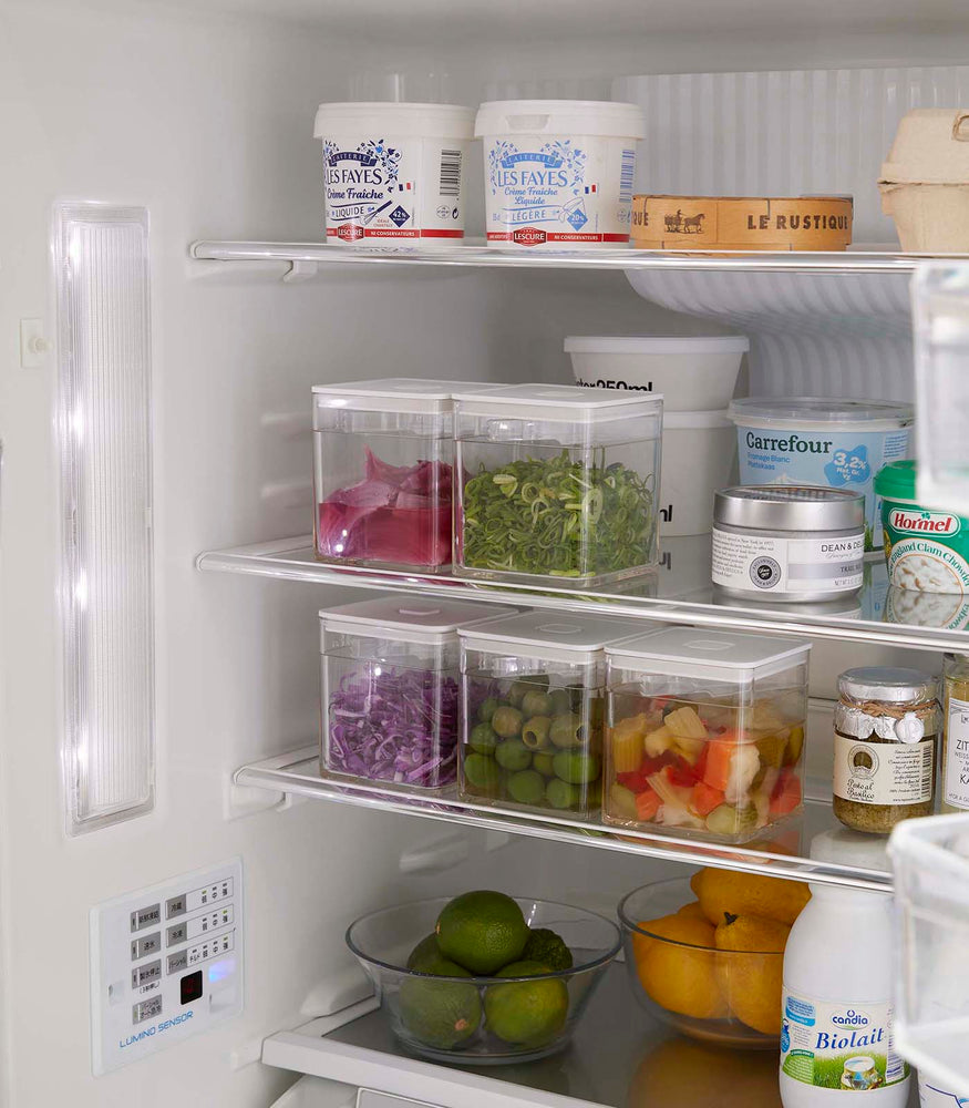 View 6 - White Vacuum-Sealing Food Container w. Tongs stacked in the fridge and holding food items by Yamazaki Home.