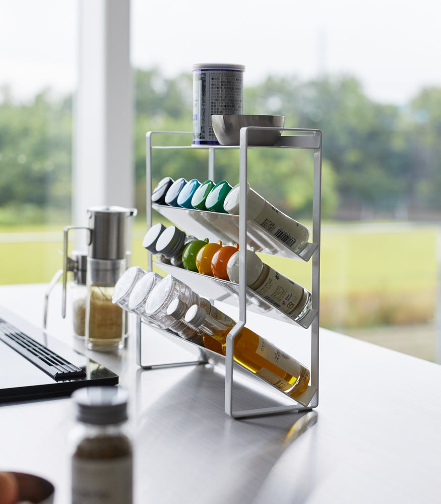 View 4 - Side view of a White Four-Tier Slim Spice Rack by Yamazaki Home neatly organized with spices and oil bottles on a light kitchen countertop.