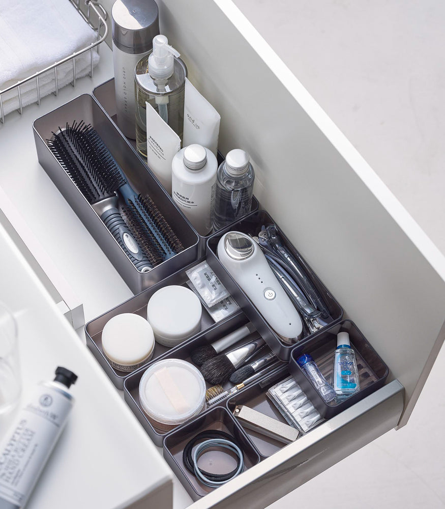 View 62 - Four different sizes of stackable clear organizers in black—small, medium, large, and deep—are neatly placed in a bathroom drawer. Made from transparent material, they accommodate items like brushes and sanitary products, showcasing their clarity and stackability.