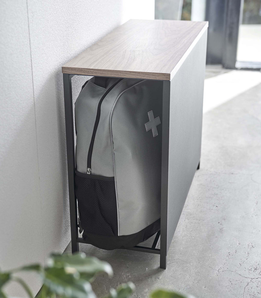 View 12 - Black Yamazaki Discreet Entryway Storage Shelf against a wall with a backpack inside