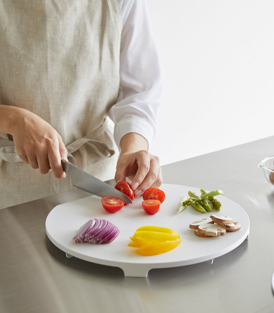 View 4 - A white Yamazaki Round Magnetic Cutting Board being used to cut vegetables.