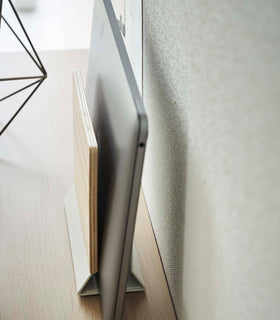 A side-view profile of a narrow wooden stand with a white metal base holding a closed laptop. view 6