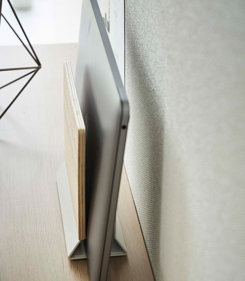 A side-view profile of a narrow wooden stand with a white metal base holding a closed laptop.