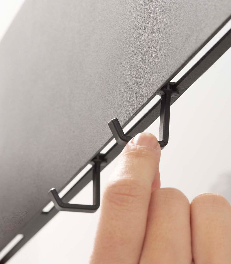 Closeup of adjustable hooks on the bottom of a Yamazaki black Magnetic Wall Panel